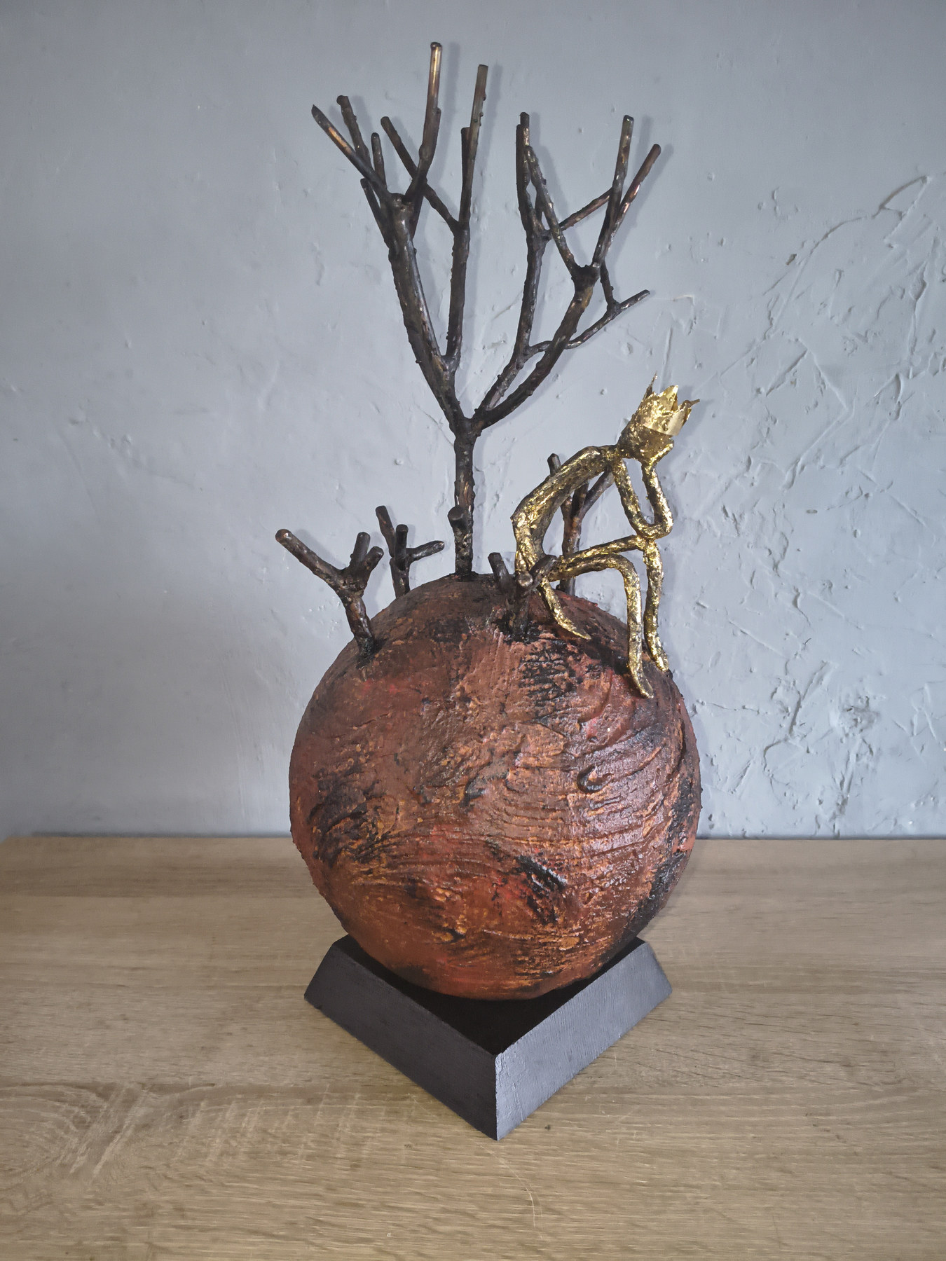 Metal sculpture with a rust-coloured sphere, bare tree branches and a small gold-toned figure, by Dan'Art.