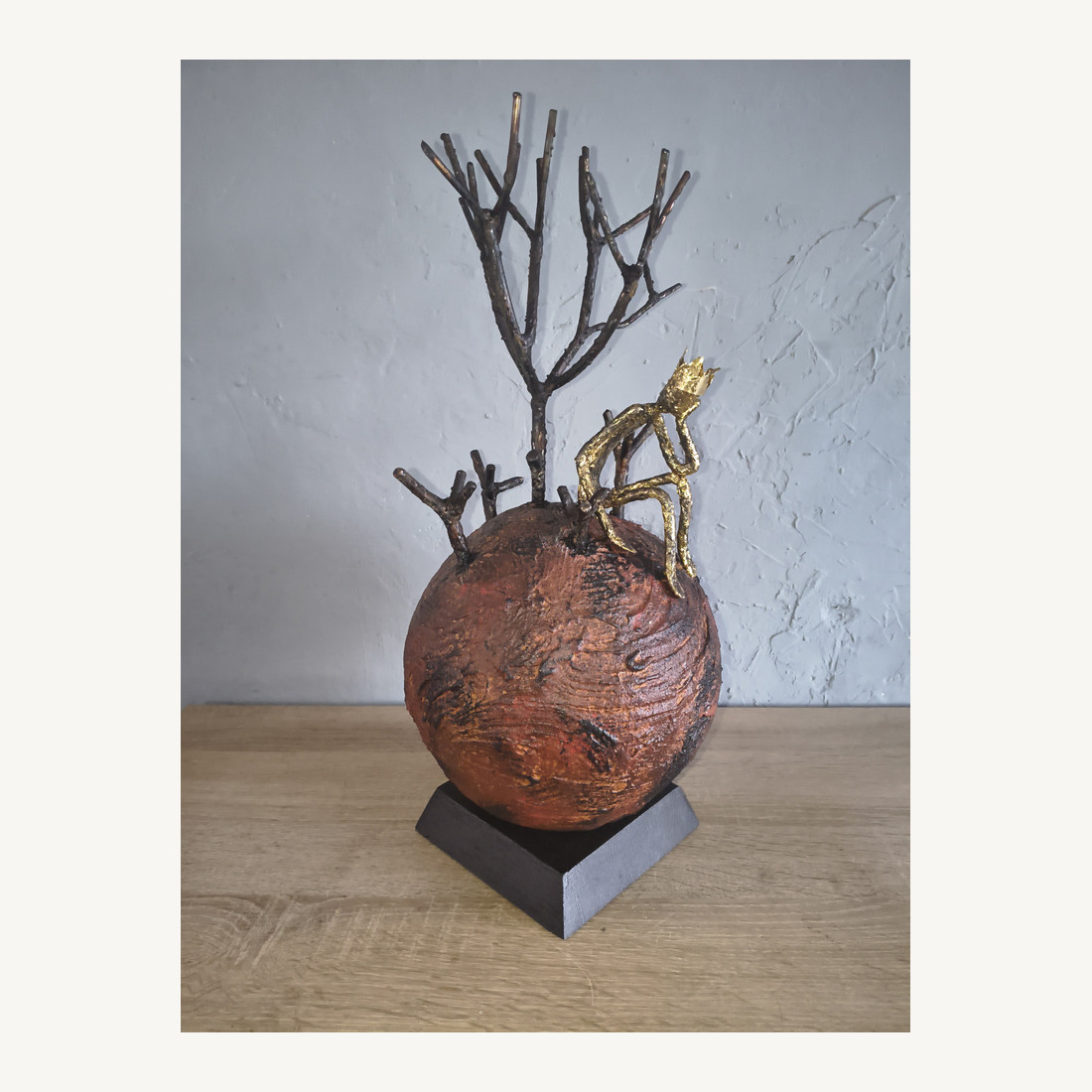 Artwork by Dan'Art featuring a rust-coloured sphere, a bare metal tree and a small gold-toned figure; not a portrait of the artist.