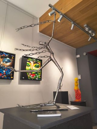 Welded steel figure with extended chain-like limbs, displayed on a pedestal in an exhibition space, by Dan'Art.