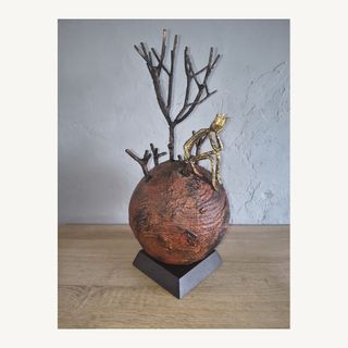 Artwork by Dan'Art featuring a rust-coloured sphere, a bare metal tree and a small gold-toned figure; not a portrait of the artist.