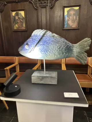 A blue-grey fish sculpture exhibited in front of carved wooden panelling in Sint-Denijskerk